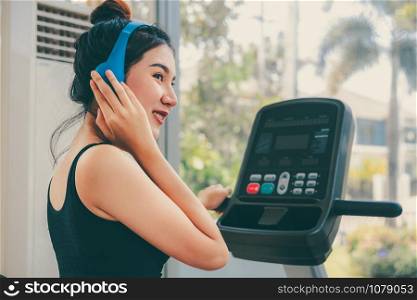 Young woman runner listens to music and runs on treadmill in fitness gym class. Healthy lifestyle concept.