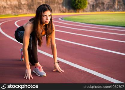 Young woman runner prepare to race on athletics track.