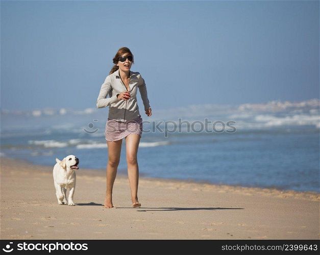 Young woman running and playing with her cute labrador retriever puppy 