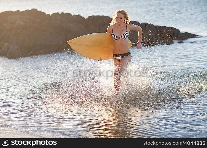 Young woman running in sea with surfboard