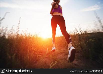Young woman running on a rural road at sunset in summer field. Lifestyle sports background