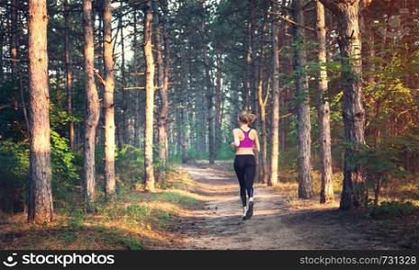 Young woman running on a rural road at sunset in summer forest. Lifestyle sports background