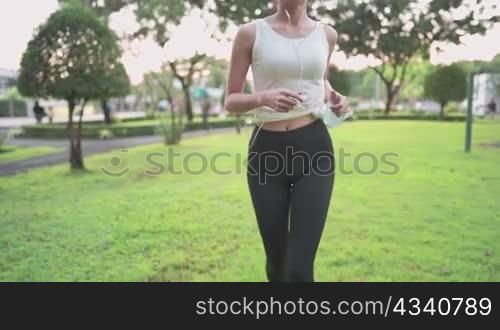 Young woman running on the green grass lawn inside public park during afternoon work out routine, protection from virus, holding protective face mask, medical condition, stay strong pandemic crisis
