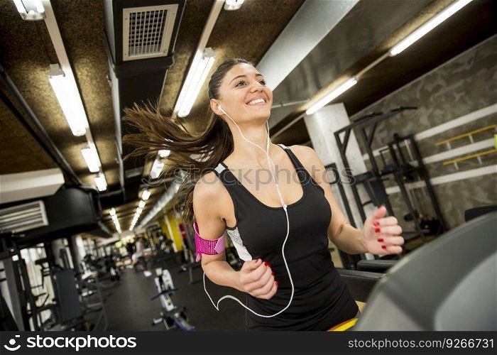 Young woman running on the treadmill and listening to music at the gym