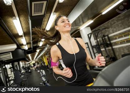 Young woman running on the treadmill and listening to music at the gym