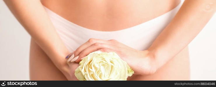Young woman’s hands holding a white flower covering epilate bikini zone isolated on white studio background. Concept of female health, reproductive, gynecology. Hands holding flower covers bikini zone