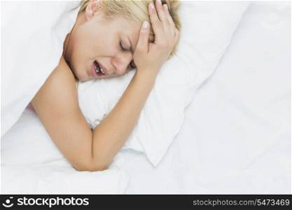 Young woman screaming while suffering from headache in bed