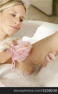 Young woman scrubbing her leg with a bath sponge in a bathtub