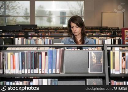 Young woman searching through the books in several bookshelves in a public library