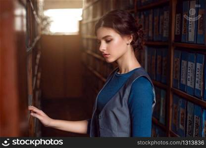 Young woman selecting book from library shelf. Knowledge, education and studying concept.. Young woman selecting book from library shelf.