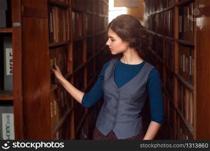 Young woman selecting book from library shelf. Knowledge, education and studying concept.. Young woman selecting book from library shelf.