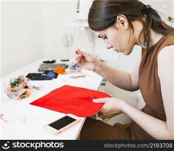young woman sewing red cloth with needle