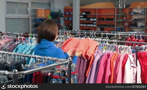 Young woman shopping for clothes in a clothing store, choosing children&acute;s jacket