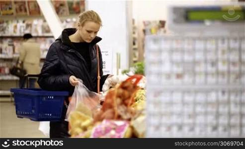 Young woman shopping in supermarket and choosing fresh vegetables, digital scales in foreground. Shot with changing focus