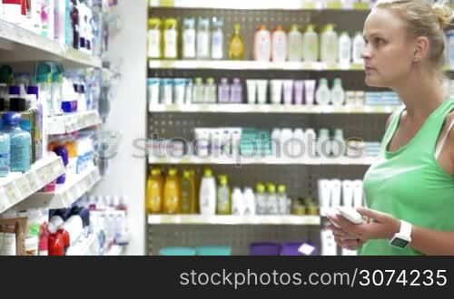 Young woman shopping in the store. She taking some cream tubes and bath salts in the beauty care section. Great assortment of body care goods on the shelves
