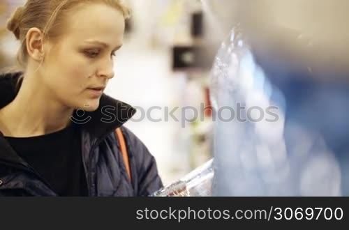 Young woman shopping in the supermarket. She choosing a bottle of mineral water and putting it in her shopping basket