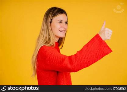 Young woman showing a thumb up to someone while standing against isolated background.