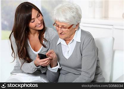 Young woman showing how to use mobile phone to grandmother