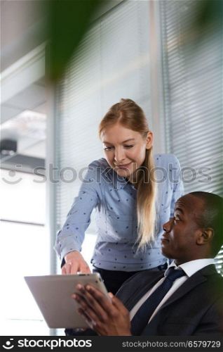 Young woman showing something on digital tablet to male colleague in office