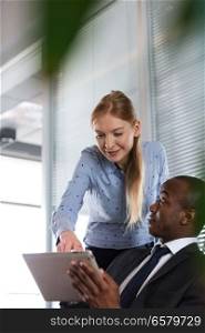 Young woman showing something on digital tablet to male colleague in office