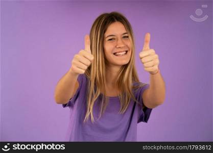 Young woman showing thumbs up to camera and smiling while standing against isolated background.