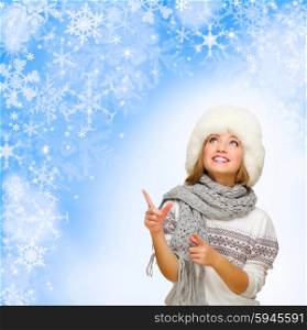 Young woman shows pointing gesture on blue snowy background