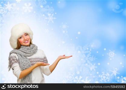 Young woman shows pointing gesture on blue snowy background