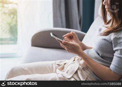 Young woman siiting on sofa and using smart phone at home