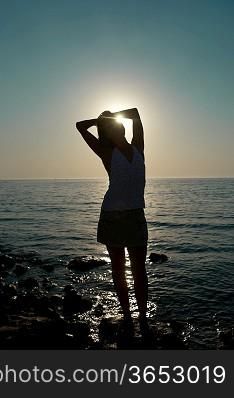 Young woman silhouette against blue sea and sunset
