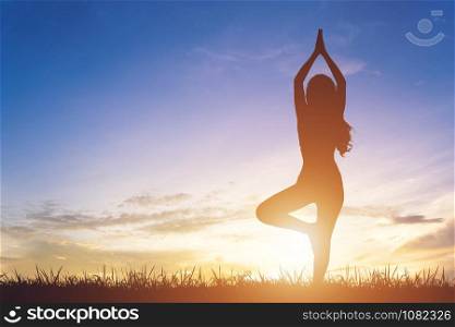 Young woman silhouette practicing yoga on sunrise sky background.