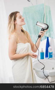 Young woman singing while drying hair in bathroom