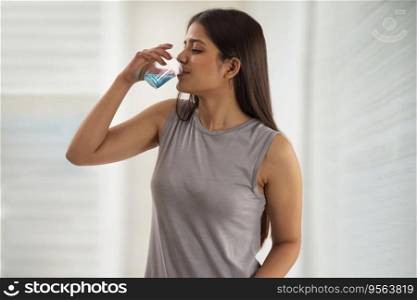 Young woman sipping from a glass of mouthwash
