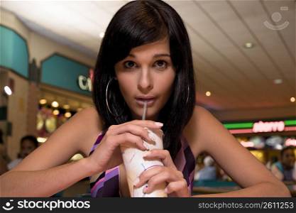 Young woman sipping soft drink in mall food court