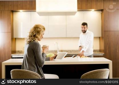 Young woman sits at the kitchen table while man preparing food