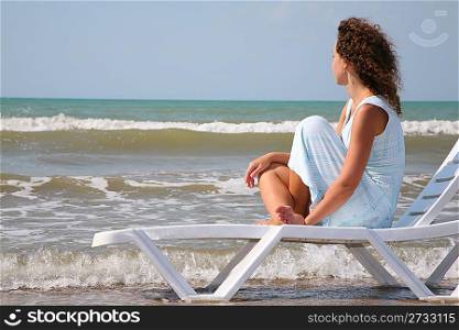 young woman sits in the chaise lounge on the edge of the sea