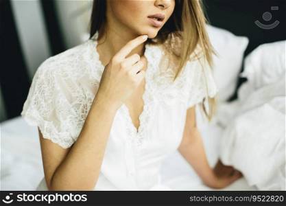 Young woman sits on a bed with white linen