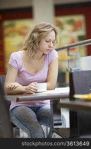 Young woman sits with a cup reading a magazine