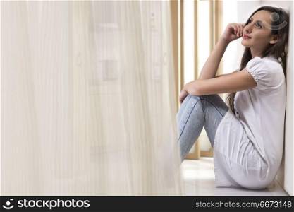 Young woman sitting against white wall at home