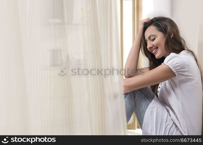 Young woman sitting against white wall at home