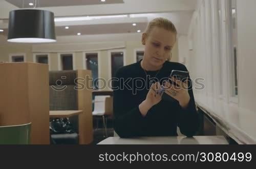 Young woman sitting alone in cafe and browsing social media on mobile