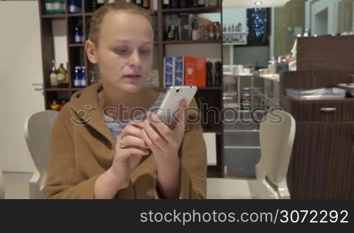 Young woman sitting alone in cafe and chatting on the smart phone while drinking coffee