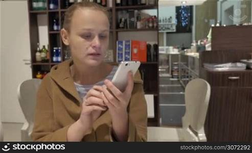 Young woman sitting alone in cafe and chatting on the smart phone while drinking coffee