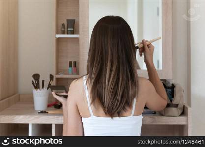 Young woman sitting and doing makeup in front of mirror in dressing room