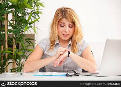 Young woman sitting and looking on hand watch in the office