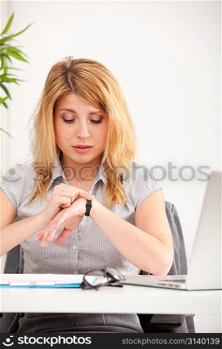 Young woman sitting and looking on hand watch in the office
