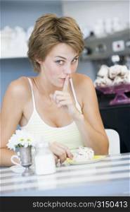 Young woman sitting at a table drinking tea and eating a sweet treat