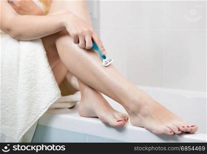 Young woman sitting at bathroom and shaving legs
