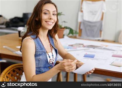 Young woman sitting at desk in creative office. Smiling young designer sitting at desk in creative office