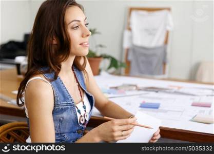 Young woman sitting at desk in creative office. Smiling young designer sitting at desk in creative office