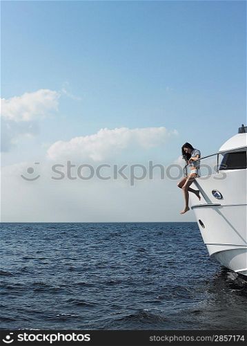 Young woman sitting at edge of yacht with legs dangling overboard side view